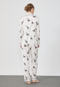 Jasny zestaw piżamowy z wzorem w żyrafy. Materiał wydaje się gładki. Góra ma kołnierzyk, a spodnie mają elastyczny pas.