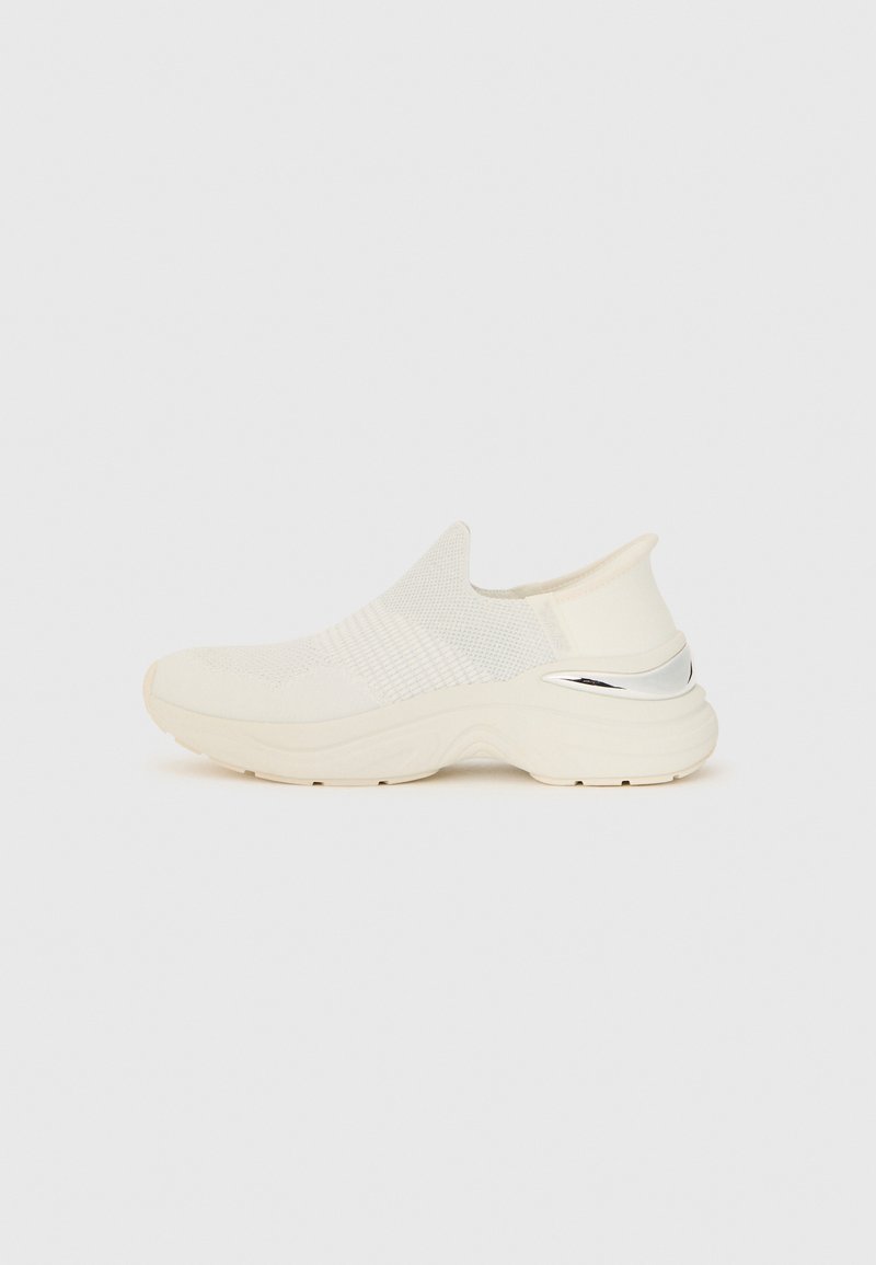 Białe dzianinowe sneakersy wsuwane z teksturowanym meshowym wierzchem, wyściełanym kołnierzem i metalicznym srebrem na pięcie. Gruba gumowa podeszwa.