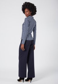 Navy patterned top with a high collar and long sleeves, featuring a geometric design. Paired with wide-leg navy trousers and black heels.