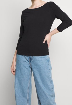 Haut noir à manches longues avec un décolleté bateau, associé à un jean bleu clair à jambes larges, présentant un buste ajusté et une coupe décontractée.