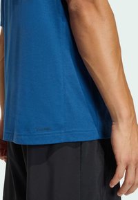 Modré bavlnené tričko s krátkymi rukávmi, okrúhlym výstrihom a logom „CLIMACOOL“ pri leme. Nosí sa s čiernymi športovými šortkami.