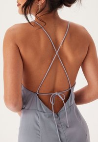 Lavendel satin klänning med låg rygg och korsettsnören. Har en knutdetalj i midjan, slät textur och minimalistisk design.