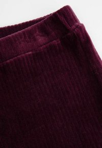 Bordowy materiał sztruksowy o pionowej, prążkowanej strukturze; charakteryzuje się miękką, pluszową powierzchnią. Materiał jest złożony na górnej krawędzi.