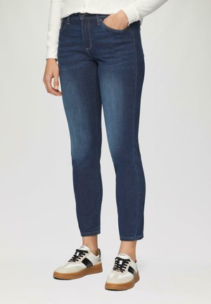 Jeans ajustés bleu marine avec un design classique à cinq poches. Associés à des baskets blanches et noires et un haut de couleur claire.
