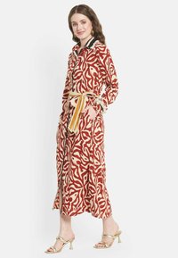 Vestito rosso e crema con motivo, colletto, maniche lunghe e vita legata. Presenta uno spacco frontale e dettagli di rifinitura intricati.