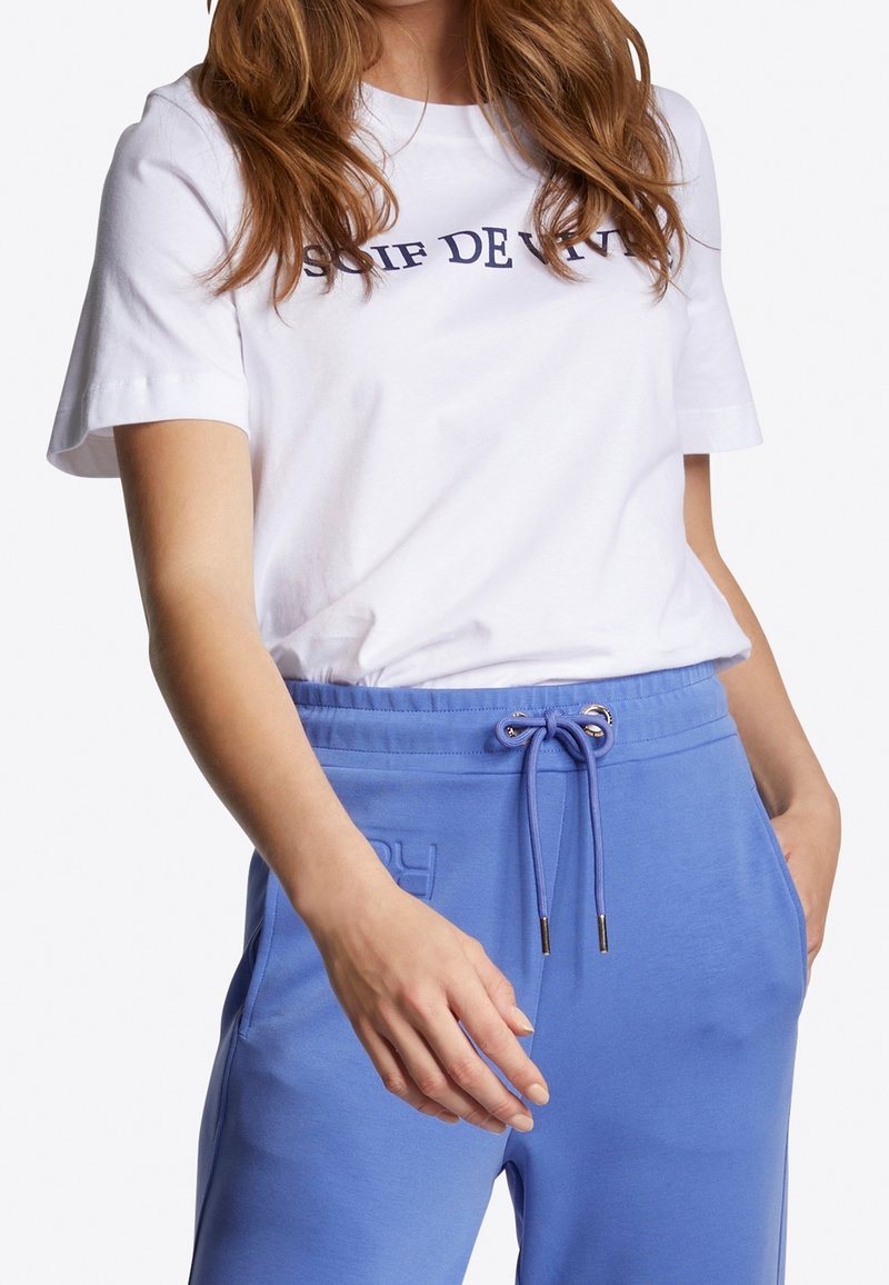 Camiseta de algodón blanco con texto en navy, acompañada de pantalones de chándal azul claro con cordón y bolsillos laterales.