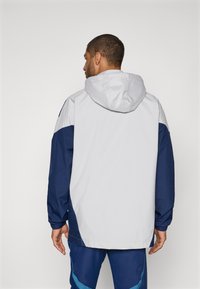 Lettvekts hettejakke i grått og marineblått, med kontrasterende paneler, elastiske mansjetter og et enkelt design, egnet for utendørs bruk.