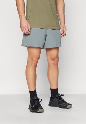 Pantalones cortos deportivos en gris claro con una textura suave, que presentan aberturas laterales. Combinados con zapatos deportivos negros y calcetines oscuros.