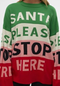 Pull avec de grands blocs de couleur vert, blanc, rose et rouge et un large texte indiquant "SANTA PLEASE STOP HERE" sur le devant.