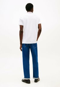 Witte polo met korte mouwen, voorzien van een geribbeld kraagje en rode accenten. Gecombineerd met blauwe spijkerbroek, opgerold bij de enkels.