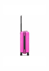 Hard-shell pink suitcase featuring a retractable black handle, four wheels, and vertical ridges on the surface for texture.
