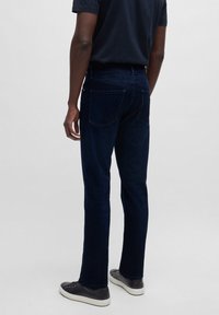 Donkerblauwe denim jeans met een slim fit, voorzien van twee achterzakken en een strakke uitstraling. Gecombineerd met een zwart shirt met korte mouwen en sneakers.