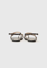 Sandálias de couro pretas com tiras finas e solas planas. O design apresenta um aspeto minimalista com um detalhe dourado no calcanhar.