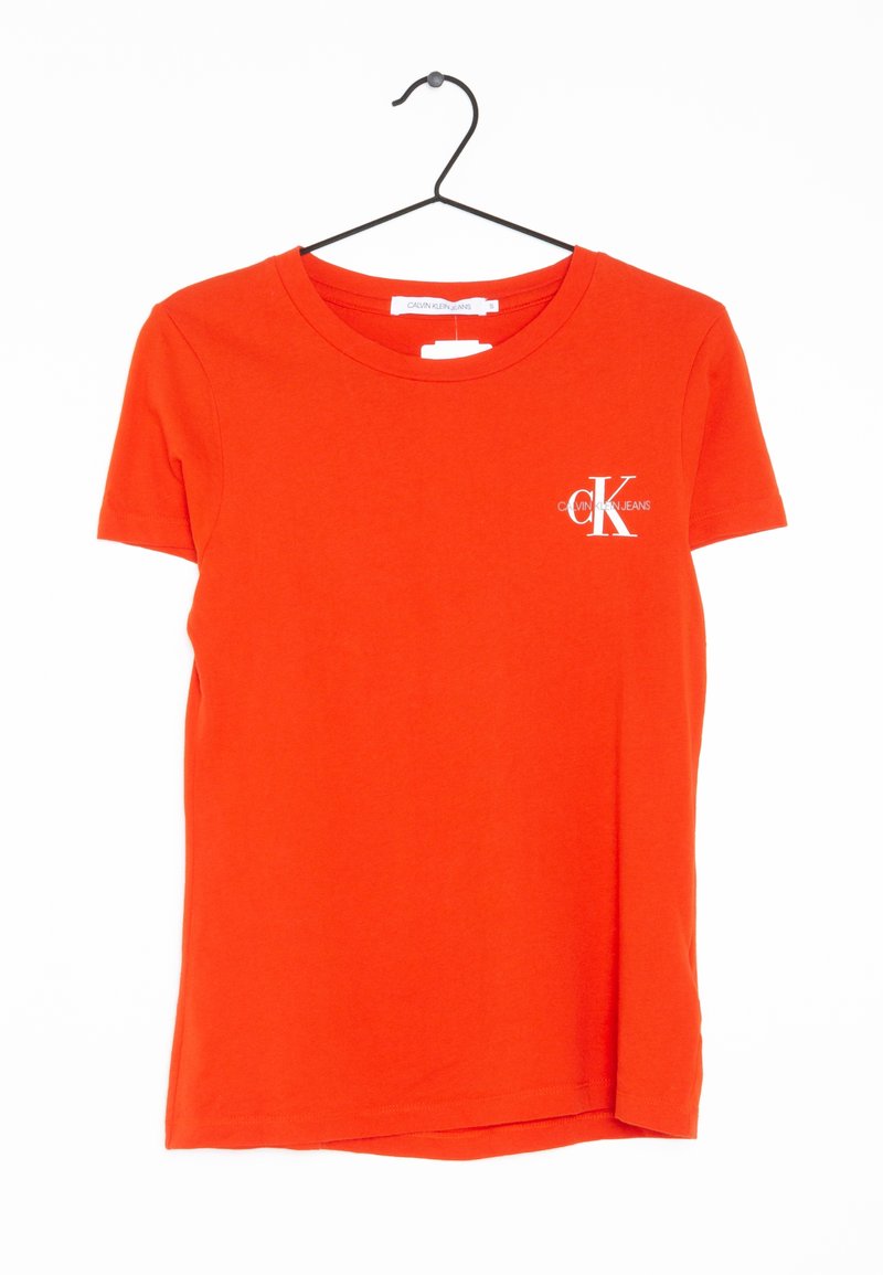 Camiseta de algodón roja con mangas cortas, escote redondo y un pequeño logo blanco en el área del pecho izquierdo. Colgada de un gancho de metal negro.