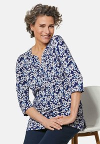 Marinebluse mit dreiviertelärmeln, die mit weißen und hellblauen Blumen verziert ist. Leicht gerafftes Design am Ausschnitt. Glattes Material.
