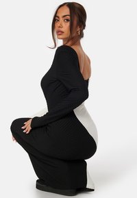 Abito aderente con un design testurizzato, nero su un lato e bianco sull'altro, con maniche lunghe e scollatura off-shoulder.