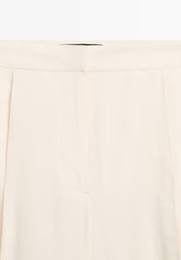 Hoch taillierte, cremefarbene Hose mit vorderen Nähten und einem verdeckten Reißverschluss im Bund.