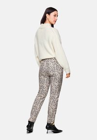 Weißer, strukturierter Strickpullover kombiniert mit beigen Leopardenmuster-Hosen und schwarzen High-Heels, von hinten betrachtet.