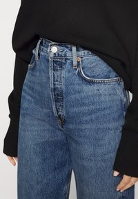 Hochgeschnittene blaue Jeans aus Denim mit ausgewaschenem Finish, mit einem vorderen Knopfverschluss und klassischem Fünf-Taschen-Design. Strukturiert. 