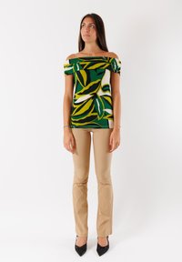 Top verde a spalle scoperte con motivi di foglie gialle e bianche, abbinato a pantaloni beige aderenti e décolleté nere a punta.