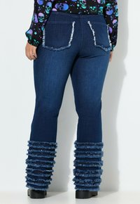 Jeans flared in denim blu scuro con orli a strisce sfilacciati e cuciture dei taschini a contrasto. Progettati con una vita aderente e gambe a stivale.
