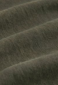 Gros plan sur un tissu vert olive plié avec une texture de sergé visible et des lignes diagonales.