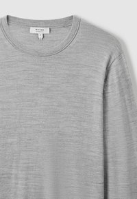 Tricou lung cu mânecă gri, cu decolteu rotund. Fabricat dintr-un material moale, texturat. Prezentând variații subtile în material.