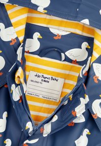 Marineblauer wasserdichter Regenmantel mit weißen Entenmuster, gelb gestreiftem Innenfutter und einem Etikett mit der Aufschrift "JoJo Maman Bébé" für 12-18 Monate.