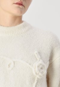 Elfenbeinfarbener, gestrickter Pullover mit geripptem Kragen, verziert mit erhöhten Blumenakzenten und einer weichen, flauschigen Textur.