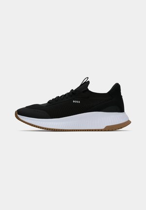 Black athletic sneakers with a textured upper, white midsole, and gum outsole. Features logo on side and pull tab on heel for ease of wear.