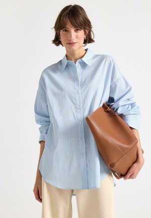 Lyseblå skjorte med knapper og hvide og beige lodrette striber, kombineret med en brun lædertaske. Casual pasform med op-rullede ærmer.