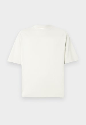 Vienkārša balta īsām piedurknēm ekipāžas kakla T-kreklu ar brīvu piegriezumu, kas attēlota uz gaiši pelēka fona.