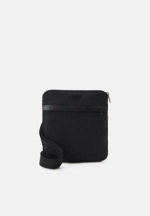 Sort nylon crossover taske med lynlås lukning, flad design og præget logo foran. Har en vævet skulderrem.