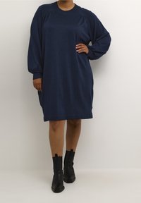Robe bleu marine à manches longues avec un col rond et des épaules froncées. Tissu doux et texturé avec une coupe décontractée et une longueur de genou.