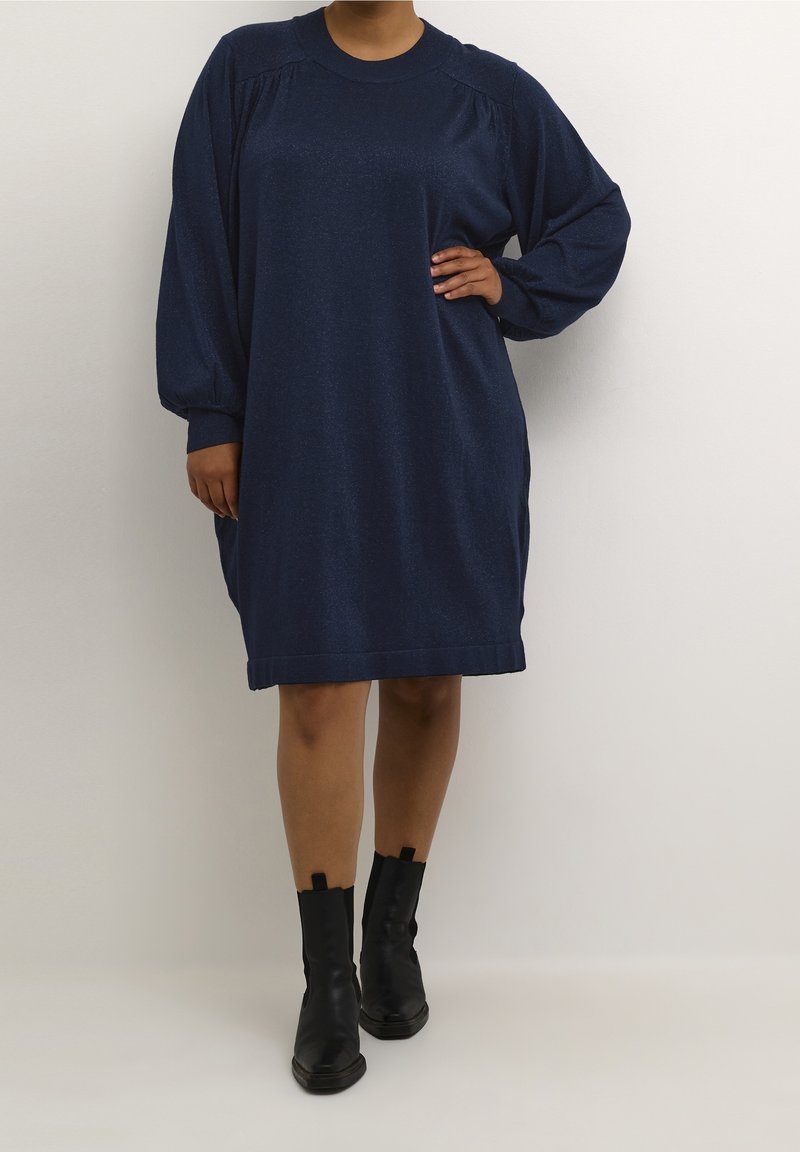 Robe bleu marine à manches longues avec un col rond et des épaules froncées. Tissu doux et texturé avec une coupe décontractée et une longueur de genou.