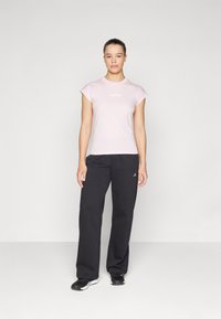 Light pink cotton t-shirt with short sleeves and white "adidas" logo. Paired with loose-fitting black sweatpants featuring white logo accents.