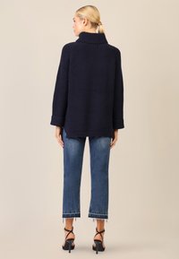Maglione a coste blu navy con colletto alto, dalla vestibilità ampia e con polsini arrotolati, abbinato a jeans azzurri cropped e tacchi neri con cinturini.