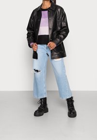 Giubbotto di pelle nera, maglione a righe in viola e nero, jeans larghi strappati in azzurro chiaro, stivali neri con tacco grosso.