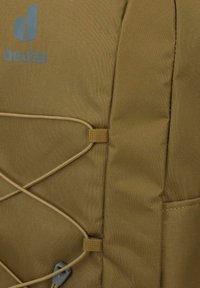 Zaino in tessuto beige con dettagli in corda elastica, dotato di un logo grigio, superficie testurizzata e hardware regolabile.