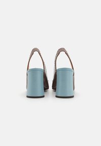 Hnědé kožené boty na podpatku s texturovaným svrškem a modrými robustními podpatky. Design zahrnuje hladký povrch a zaoblenou špičku.