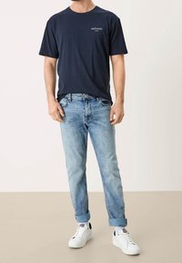 Camiseta de algodón en azul marino con el logo en blanco "reframe", combinada con unos jeans de mezclilla azul claro y zapatillas blancas, con los puños de los jeans doblados.
