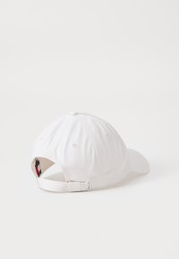 White baseball cap with a rounded crown, fabric texture, adjustable strap at the back, and branded label inside.