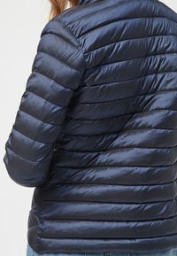 Navy puffer jacket with horizontal quilted sections and a shiny, smooth texture. Features a high collar and fitted sleeves.