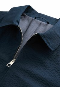 Chaqueta azul marino con una textura suave, cierre de cremallera con detalles en plata y un forro interior ligero en contraste.