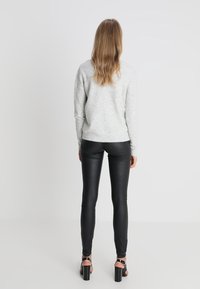 Grauer Pullover mit Rundhalsausschnitt, kombiniert mit schwarzen, enganliegenden Lederhosen und schwarzen, hochhackigen Sandalen, von hinten betrachtet.