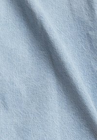 Vaaleansininen kangas, jossa on pehmeä, teksturoitu pinta. Näyttää hienovaraista, kudottua kuvioita, jotka ovat tyypillisiä denimiä. Käännetty, paljastaen syvyyttä ja liikettä.