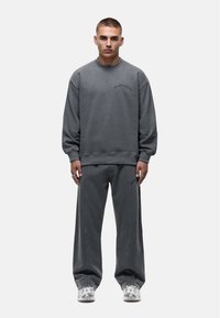 Felpa grigia e pantaloni coordinati realizzati in tessuto morbido; presenta polsini a coste, vestibilità ampia e un discreto ricamo del logo sul petto e sulla coscia.