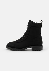 Bottes noires à la cheville en daim, avec un bout rond, un laçage à l'avant et une semelle en caoutchouc basse avec un motif texturé.