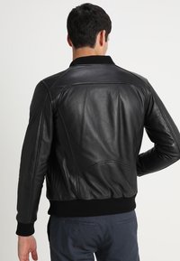 Svart läderbomberjacka med ribbad krage och ärmslut, med en mjuk yta och detaljerad sömnad på baksidan.