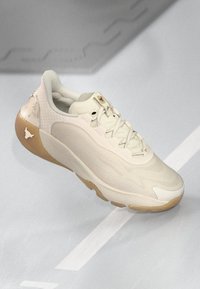 Sneaker beige chiaro con una parte superiore testurizzata, linee di design sottili, colletto imbottito e suola in gomma con un accento traslucido.